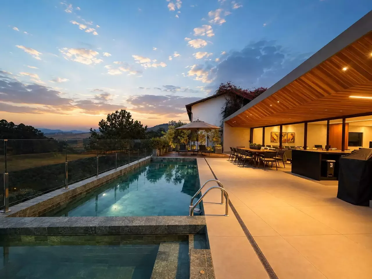Piscina e varanda iluminada diante de uma paisagem ao entardecer